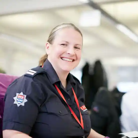 A London Fire Brigade member smiling at the camera from her desk.  